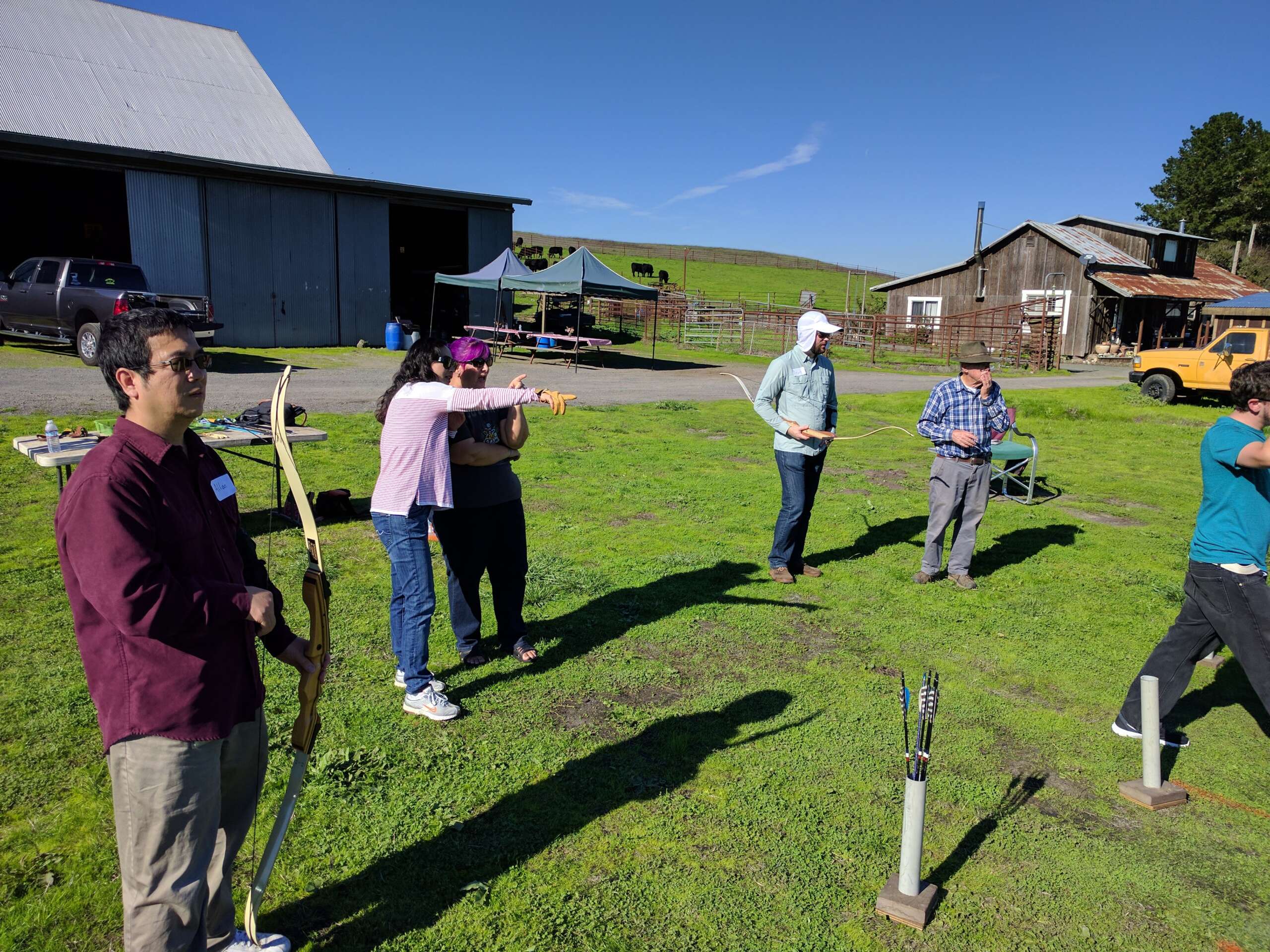 A group of people practicing archery outdoors on a sunny day.